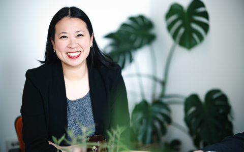 Jessica Peng sits in her office and poses for a photo. She is smiling at the camera and a monstera plant is behind her.