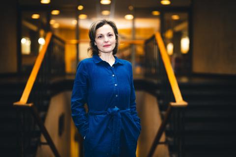 Liz Barrett stands in front of steps wearing a dark blue dress and looking at the camera.