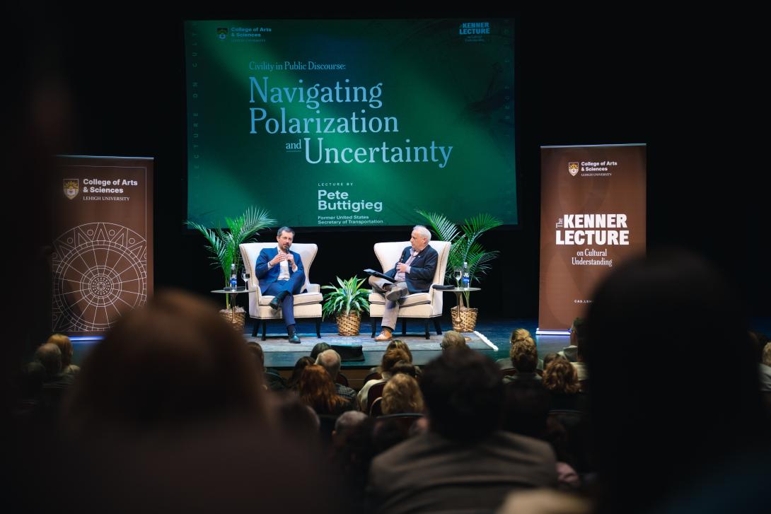 Pete Buttigieg and Ziad Munson sit on stage for a Q&A discussion. There is a screen behind them with a green graphic that reads "Navigating Polarization and Uncertainty."